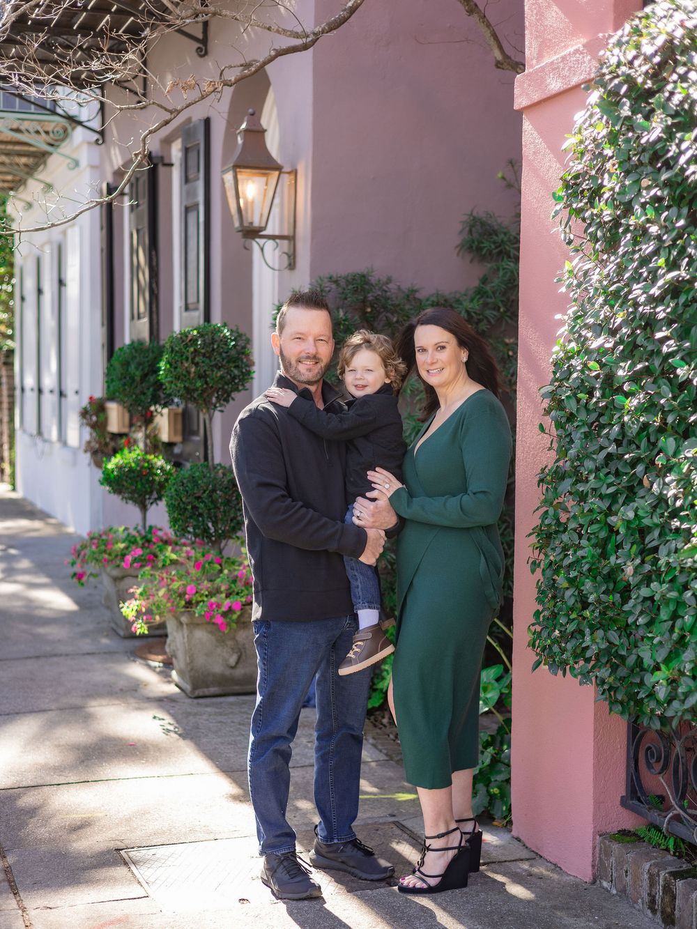 A couple poses together in a charming pink-walled courtyard with climbing vines and hanging plants.