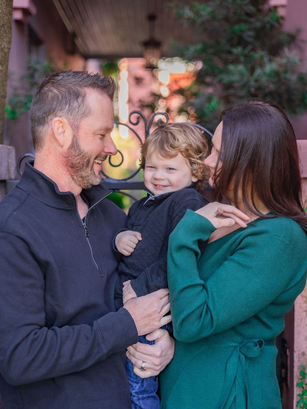 A family shares a joyful moment together outdoors, with the child laughing while being held between the adults.