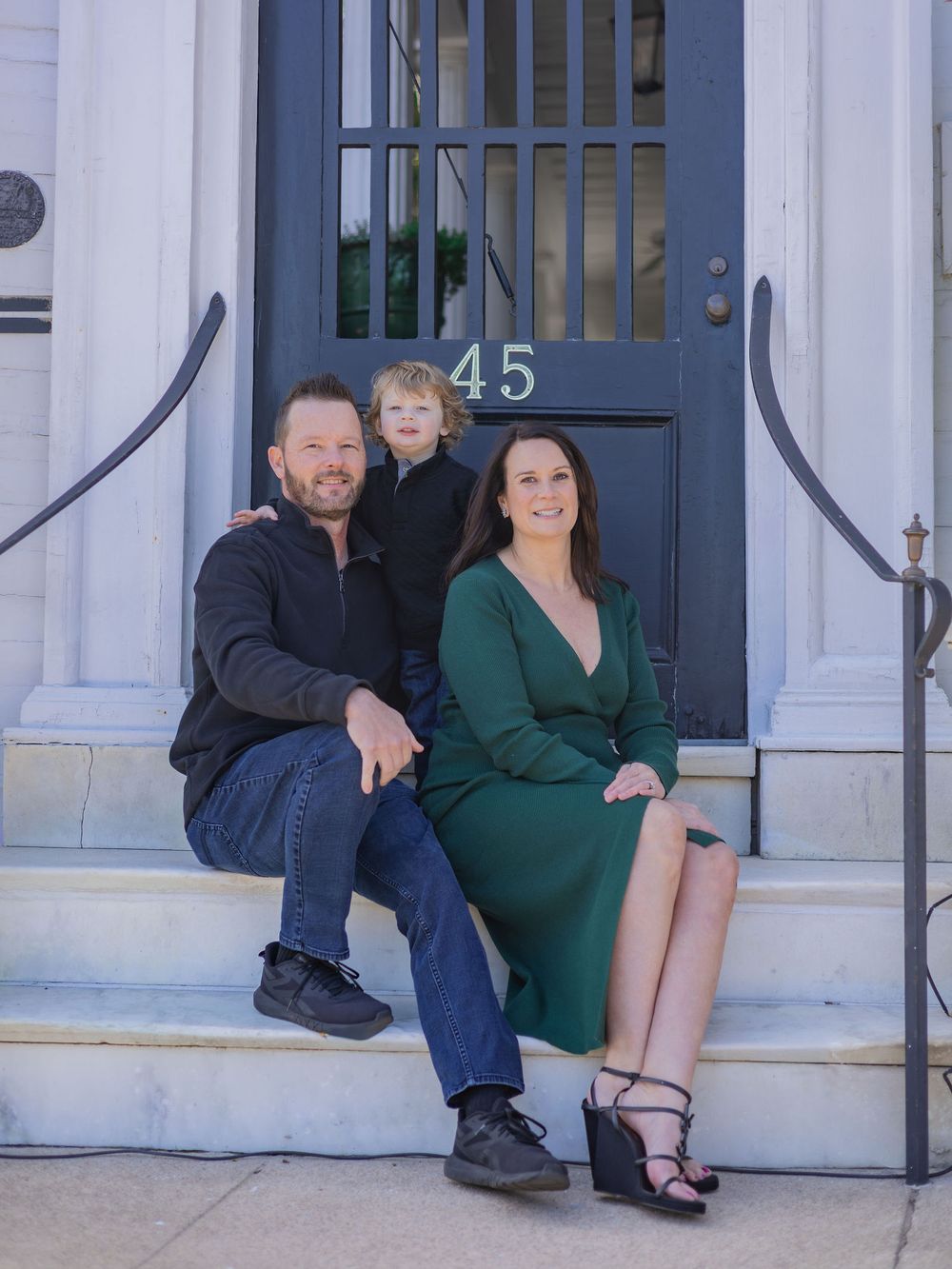 Couple in coordinated outfits sitting on white stone steps outside a building with a blue door marked 45.