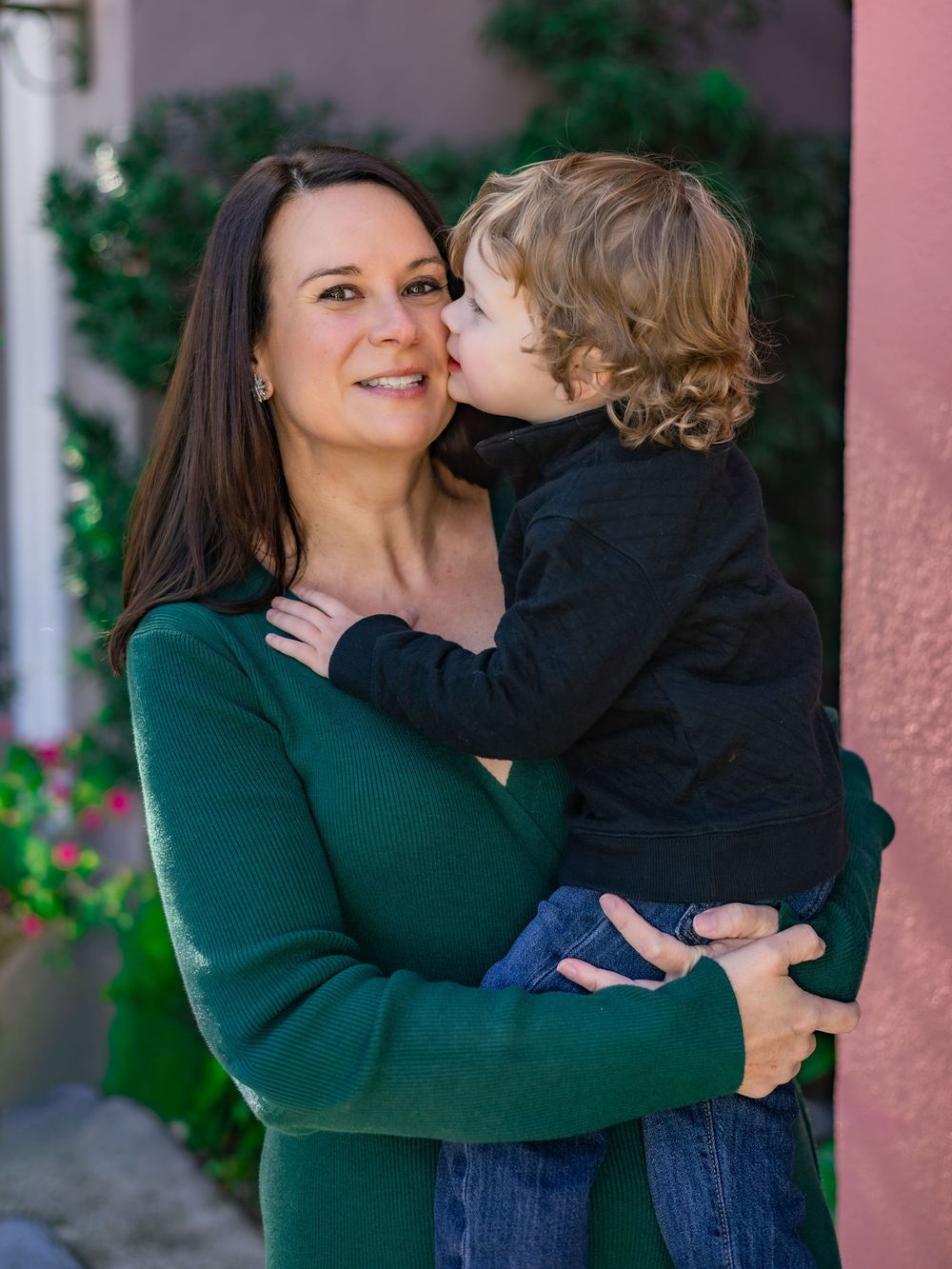A tender moment shared between parent and child wearing green and navy outfits against a pink wall backdrop.
