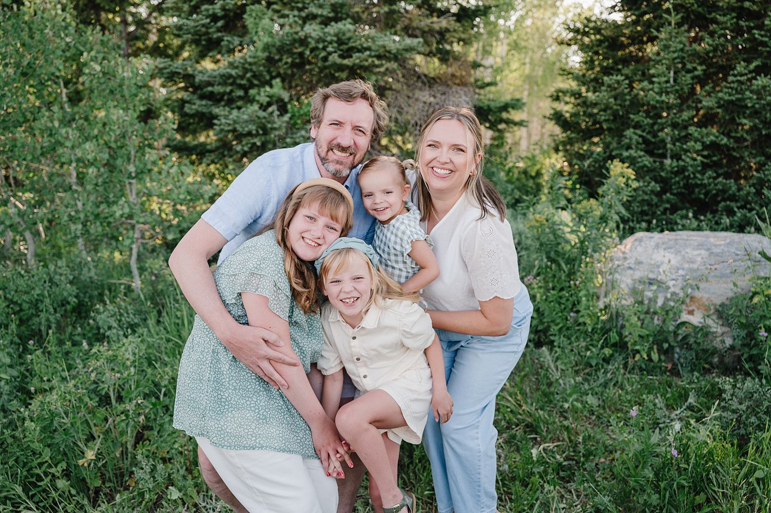 A joyful group poses together outdoors against a backdrop of green foliage and evergreen trees.