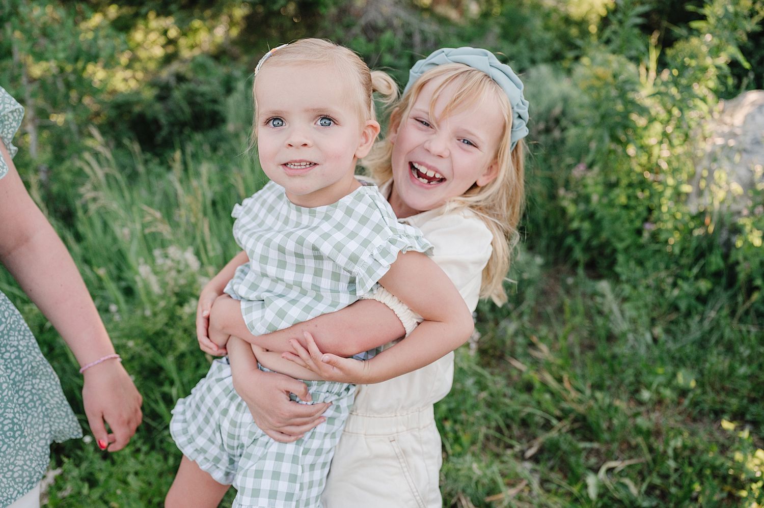 Two children embrace and laugh together while playing outdoors in a natural garden setting.