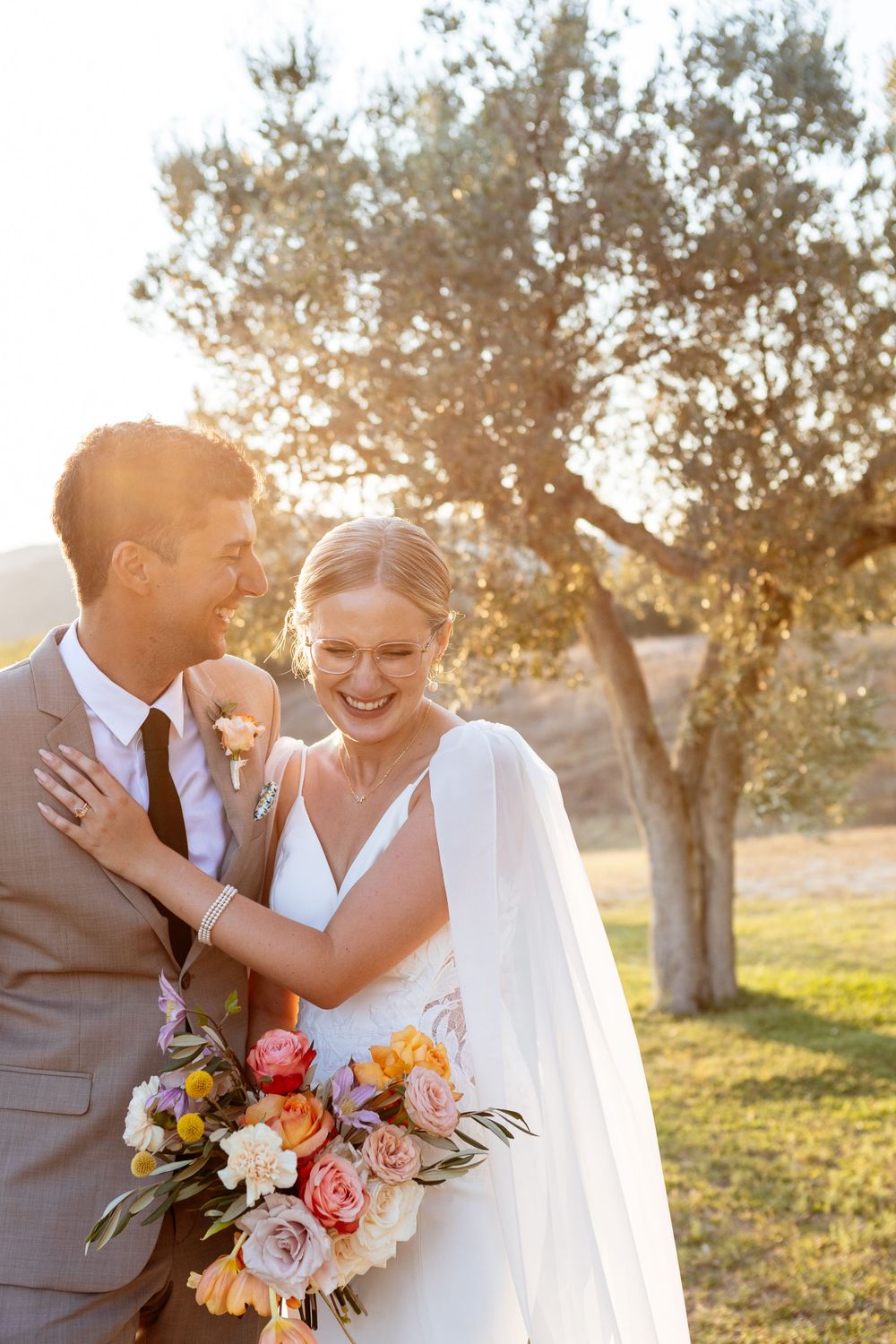 A romantic wedding couple shares a joyful moment at sunset with a gorgeous colorful bouquet at Convento di Montepozzali in Tuscany.