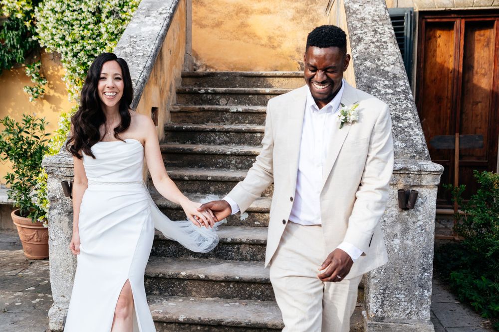A couple in wedding attire pose together on stone steps at the beautiful rustic venue of Villa Ulignano in Tuscany.
