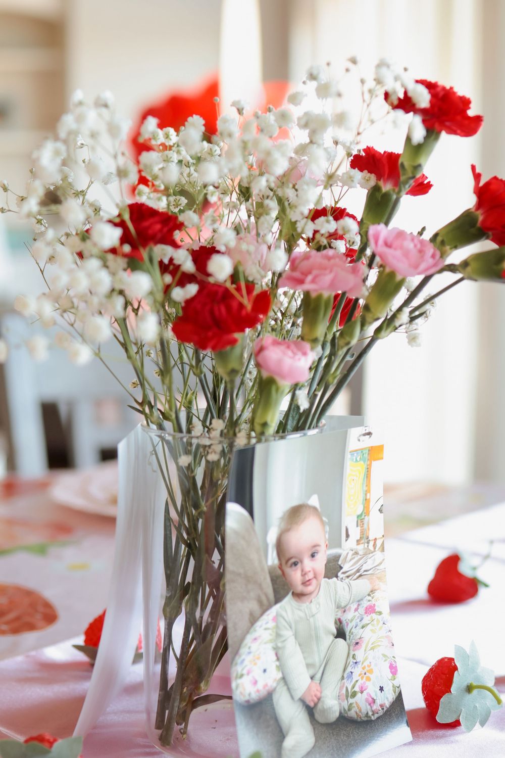 Fresh floral centerpiece with red carnations, pink flowers and baby's breath in a clear glass vase on a table.