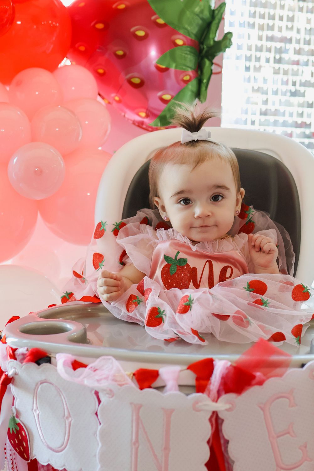 First birthday party setup with strawberry themed decorations and high chair.