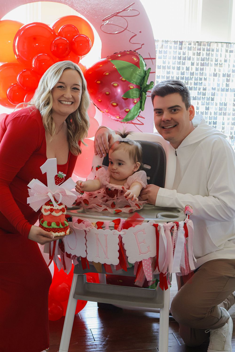 Family celebrating at a strawberry themed first birthday party with red balloons and decorations.