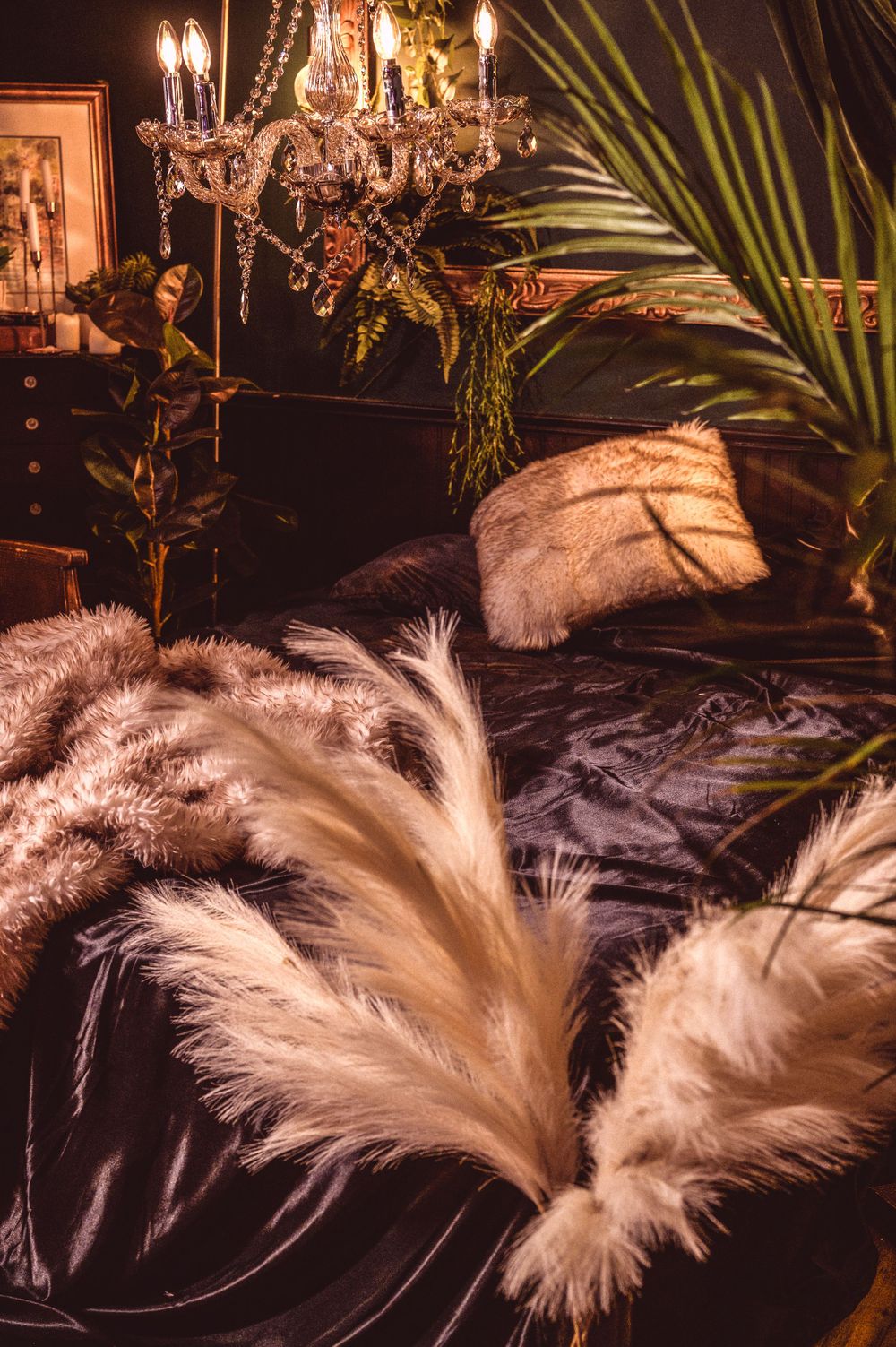 A moody interior scene with pampas grass, palm fronds and crystal chandelier creating luxurious bohemian ambiance.