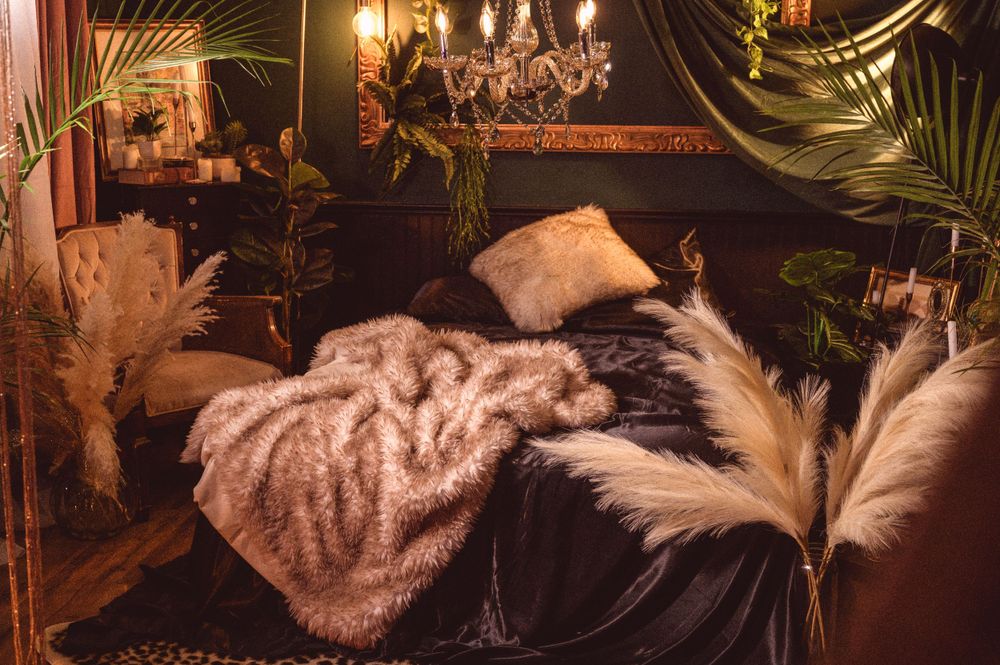 A cozy velvet lounge decorated with plush blankets, pampas grass, and hanging lights creating a romantic ambiance.
