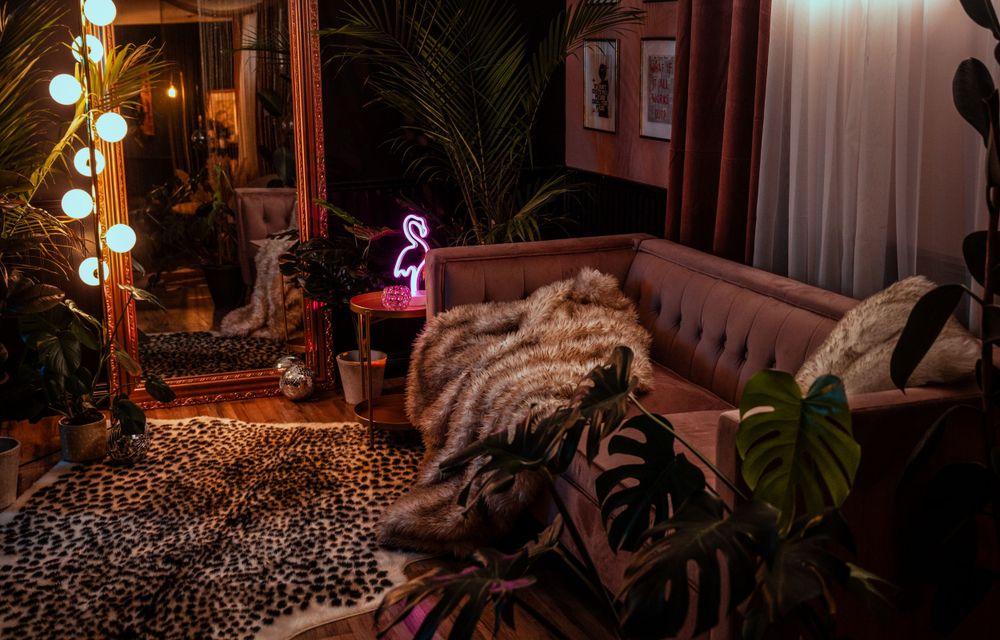 A cozy living room with leopard print rug, brown leather couch, fur throw, and neon pink lighting creates a moody ambiance.
