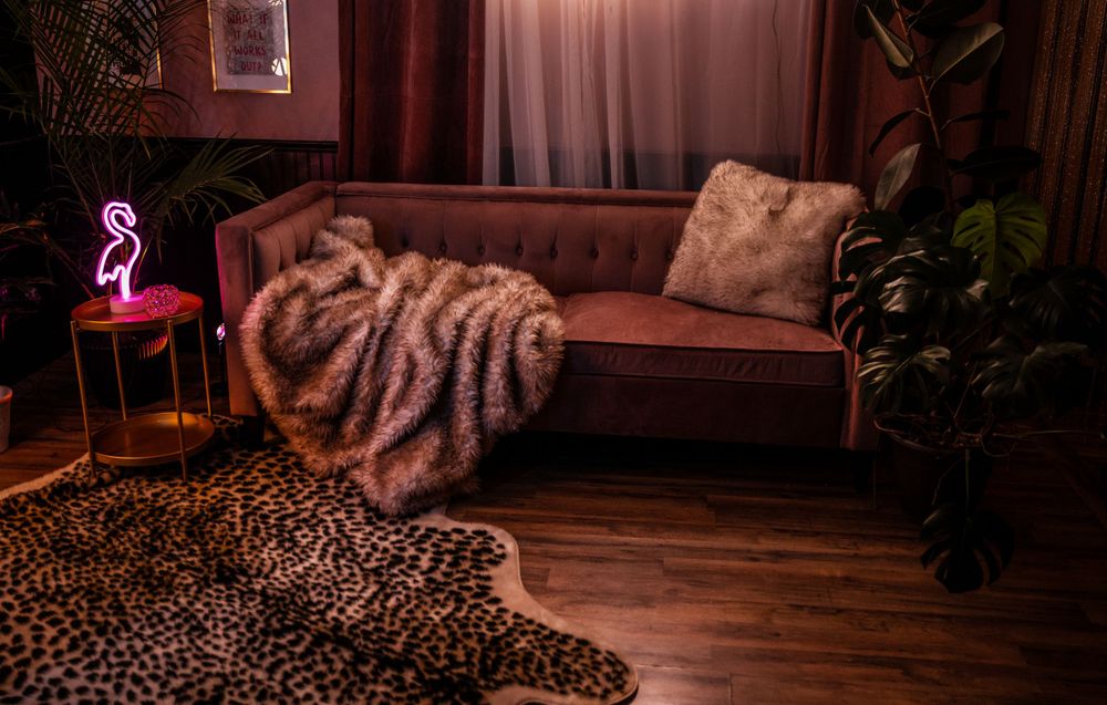 Cozy living room with brown leather couch, faux fur throw, leopard print rug, neon pink light and dark red curtains.