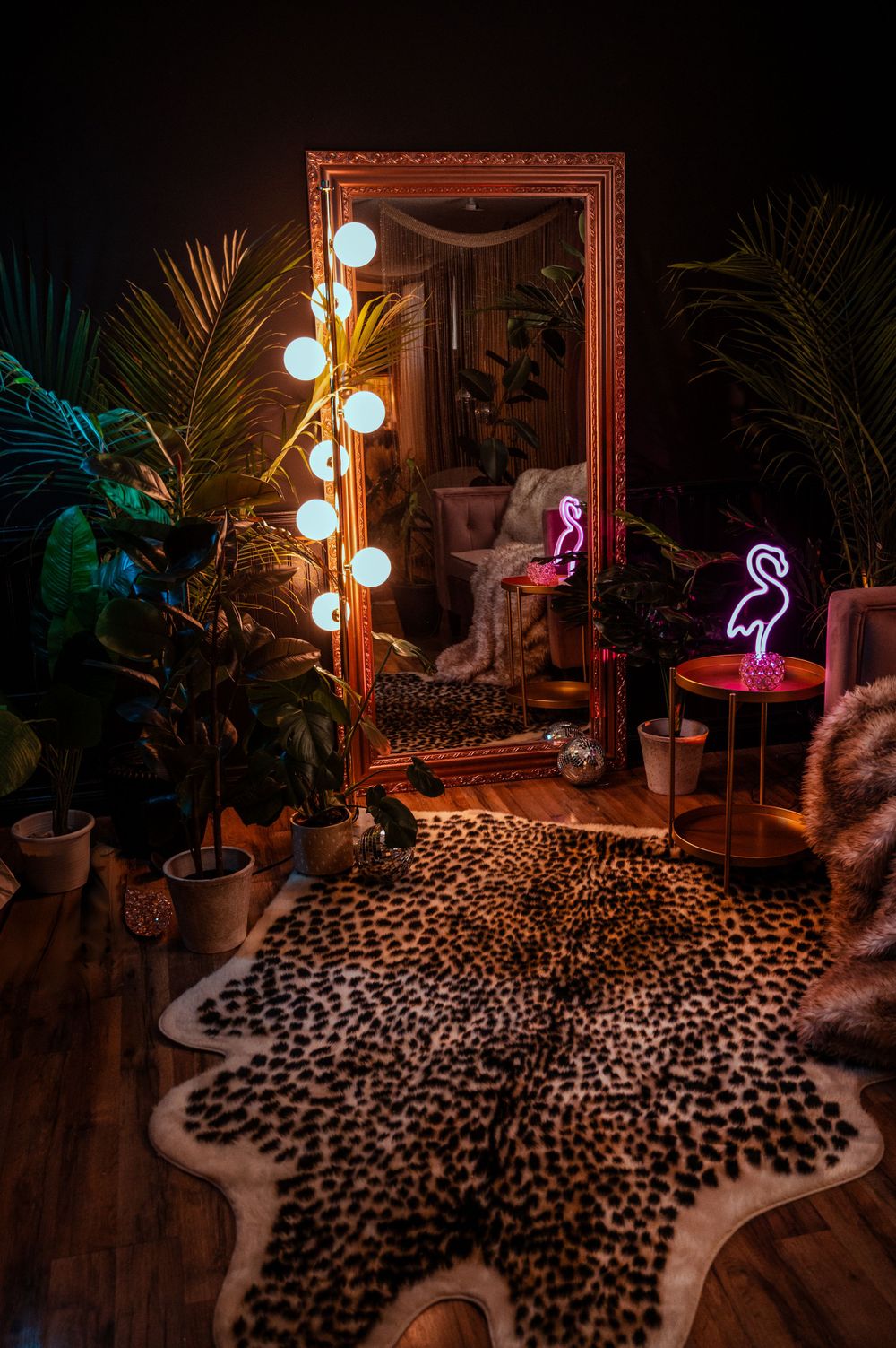 Cozy room interior with leopard print rug, vintage mirror, lighted vanity bulbs and pink neon flamingo decor.