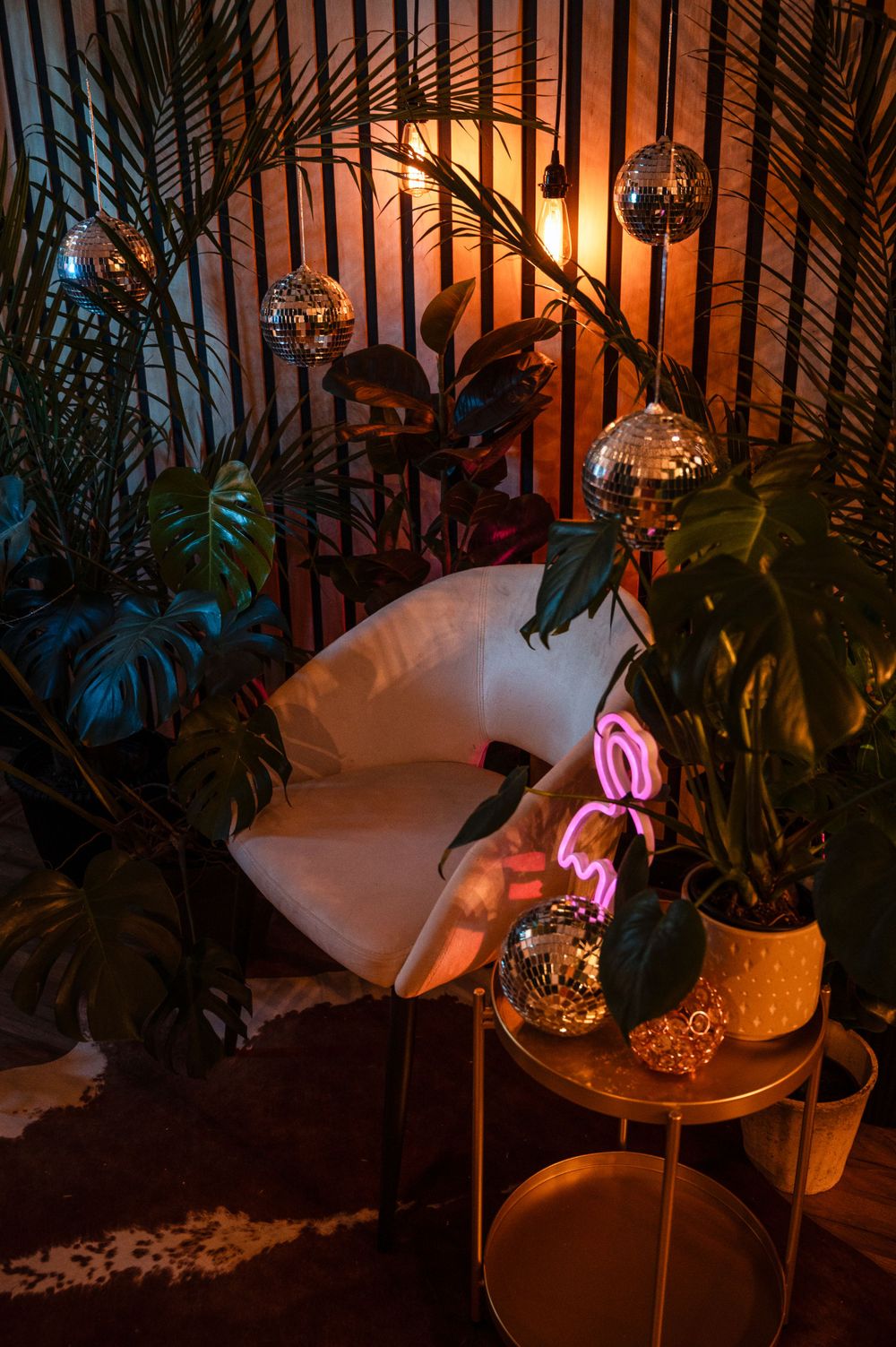Cozy corner with neon lights, disco balls, tropical plants and white cushions creating moody nighttime ambiance.