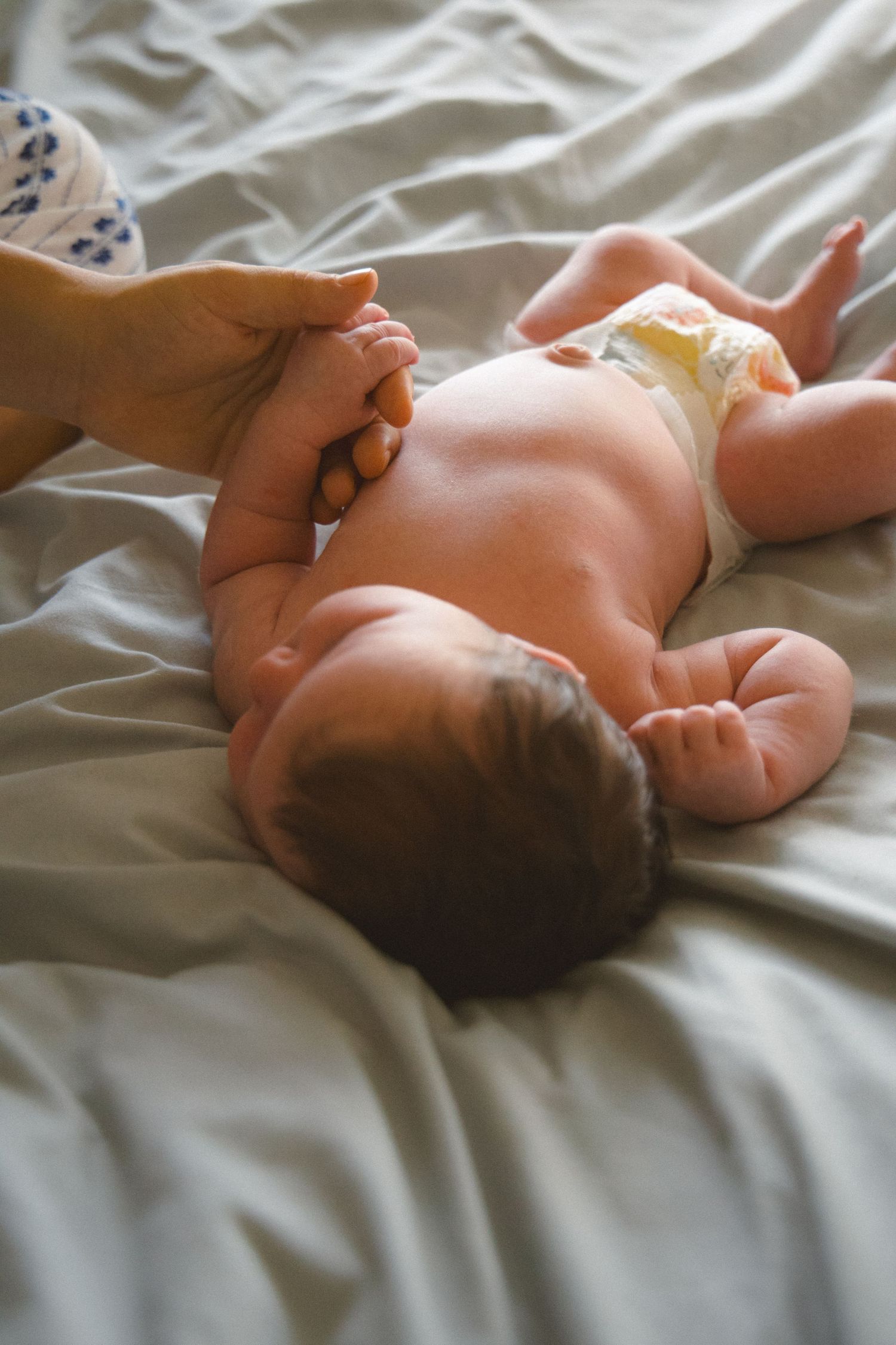 newborn holding parent finger lying on bed
