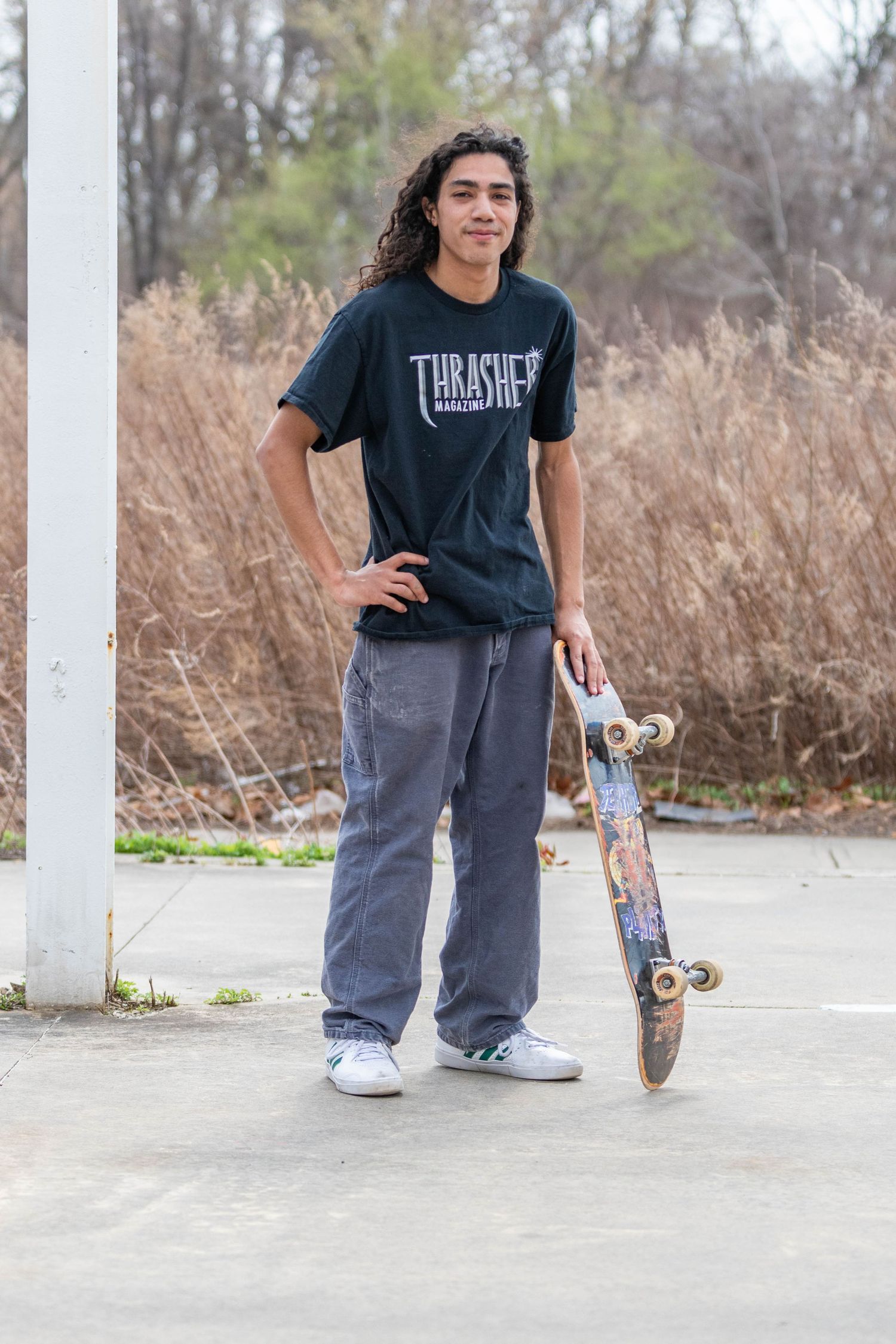 A man with long hair posing with a skateboard.