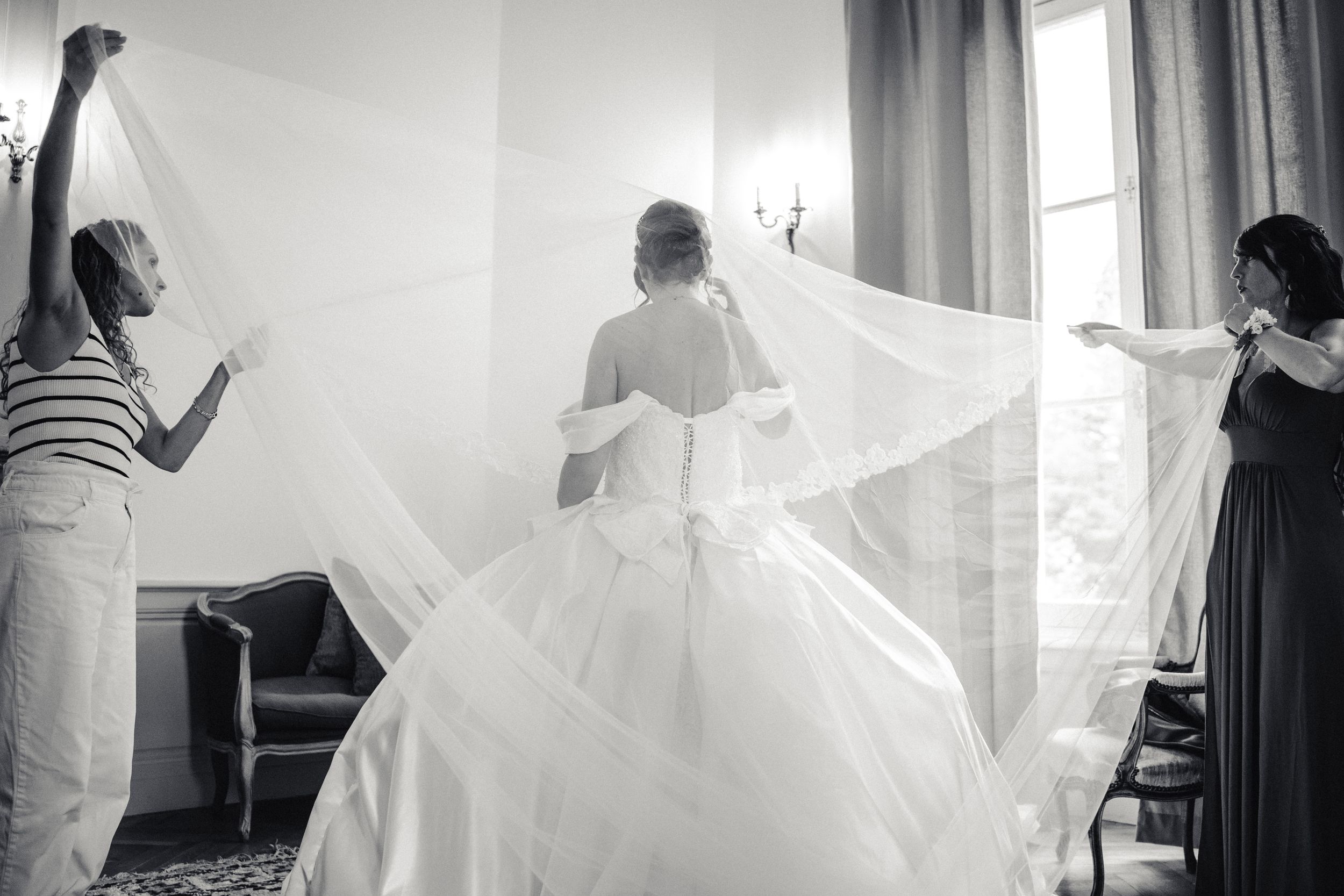 Pendant les préparatifs l'immense voile blanc de la robe de mariée style princesse est tenu par les amies dans une salle du chateau