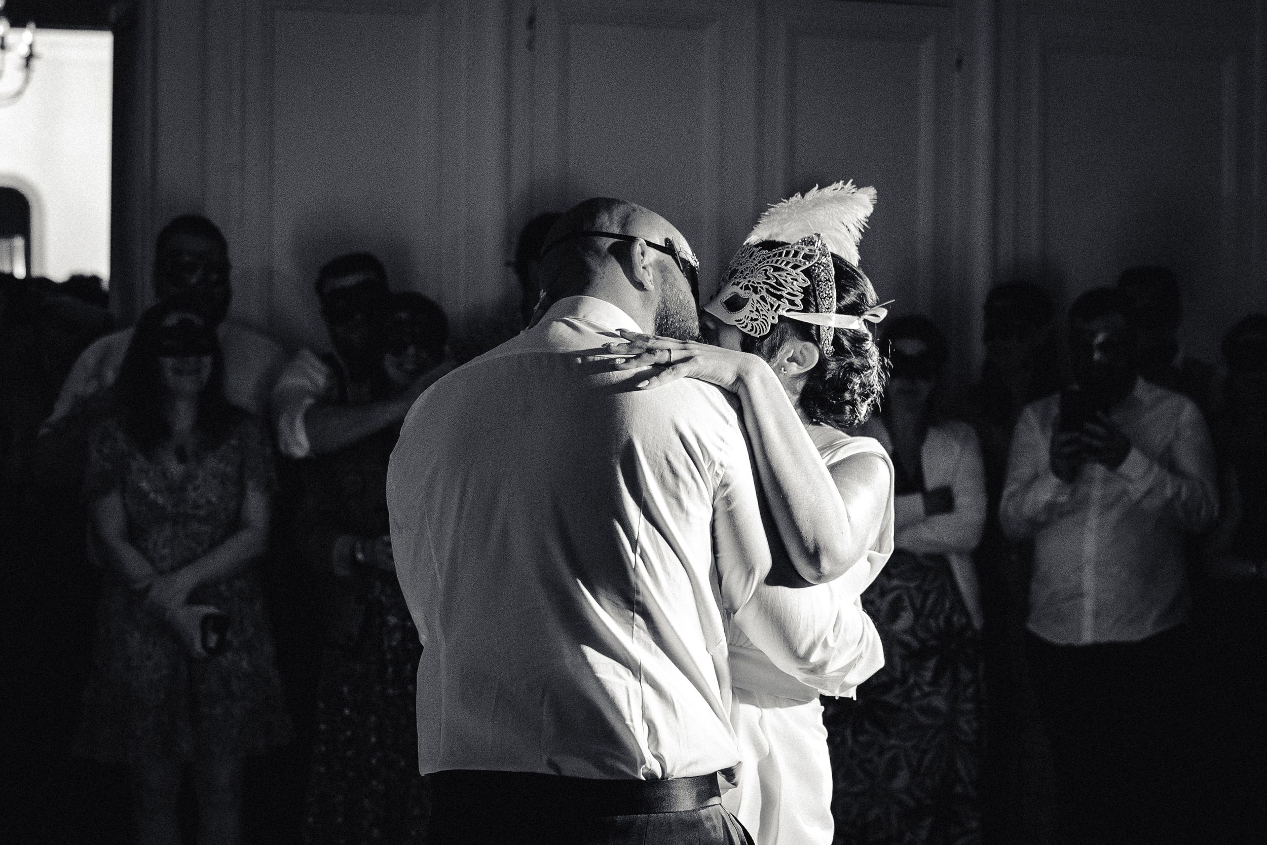 Salle de réception chateau les invités regardent la première danse ouverture de bal des mariés masqués qui s'embrassent, photo noir et blanc