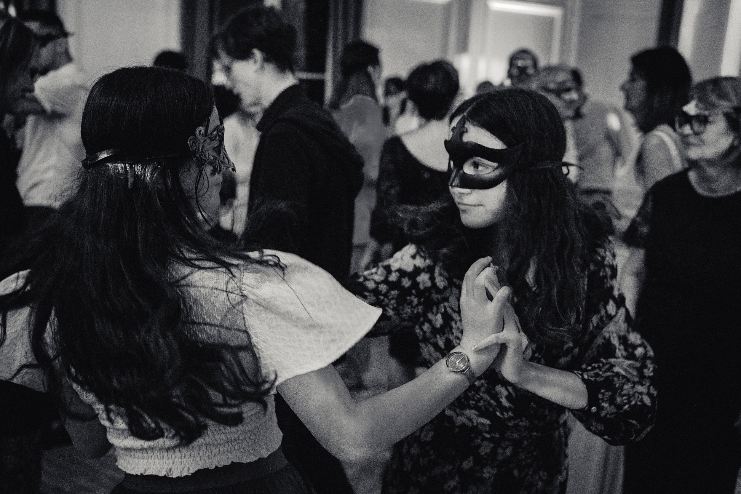 Danse de deux jeunes filles masquées qui se tiennent les mains pendant la soirée de mariage salle de réception chateau photo noir et blanc