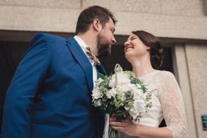 Sortie des mariés de l'église stJoseph du Havre qui se regardent en souriant, la mariée tient 1 bouquet dans les tons blancs verts hortensia