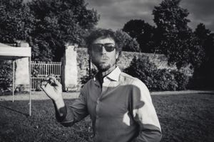 Parc du chateau lors d'un mariage, un invité avec lunettes de soleil fume une cigarette, la fumée sort de sa bouche, photo en noir et blanc