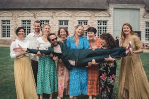 Photo de groupe de mariage, le marié costume vert lunettes de soleil est allongé tenu par plusieurs de ses témoins et ami(e)s qui sourient