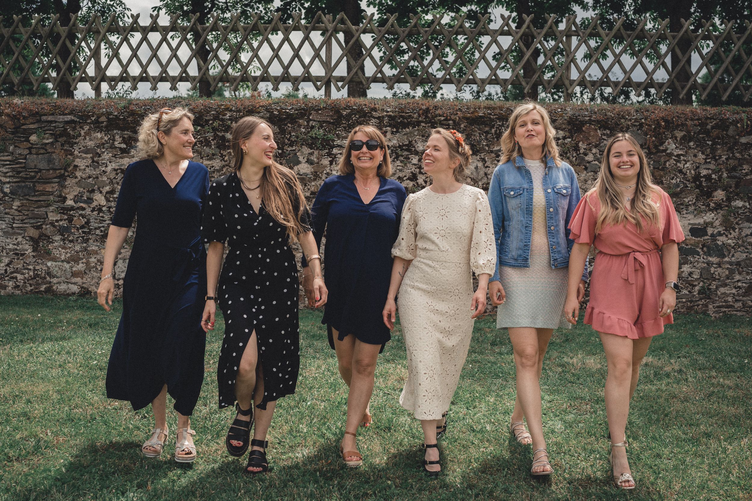 Photo de groupe de mariage, la mariée avance en ligne côte à côte avec ses témoins et amies vers la photographe dans le parc du chateau