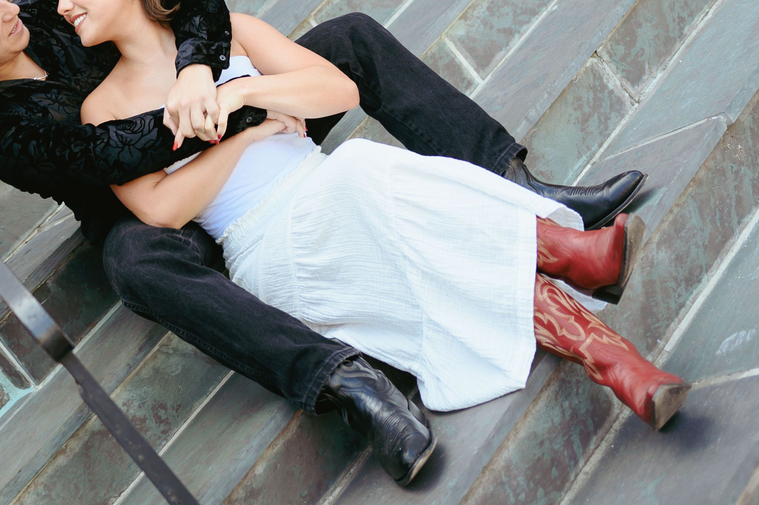 Couple in contrasting black and white outfits pose playfully on stone steps.