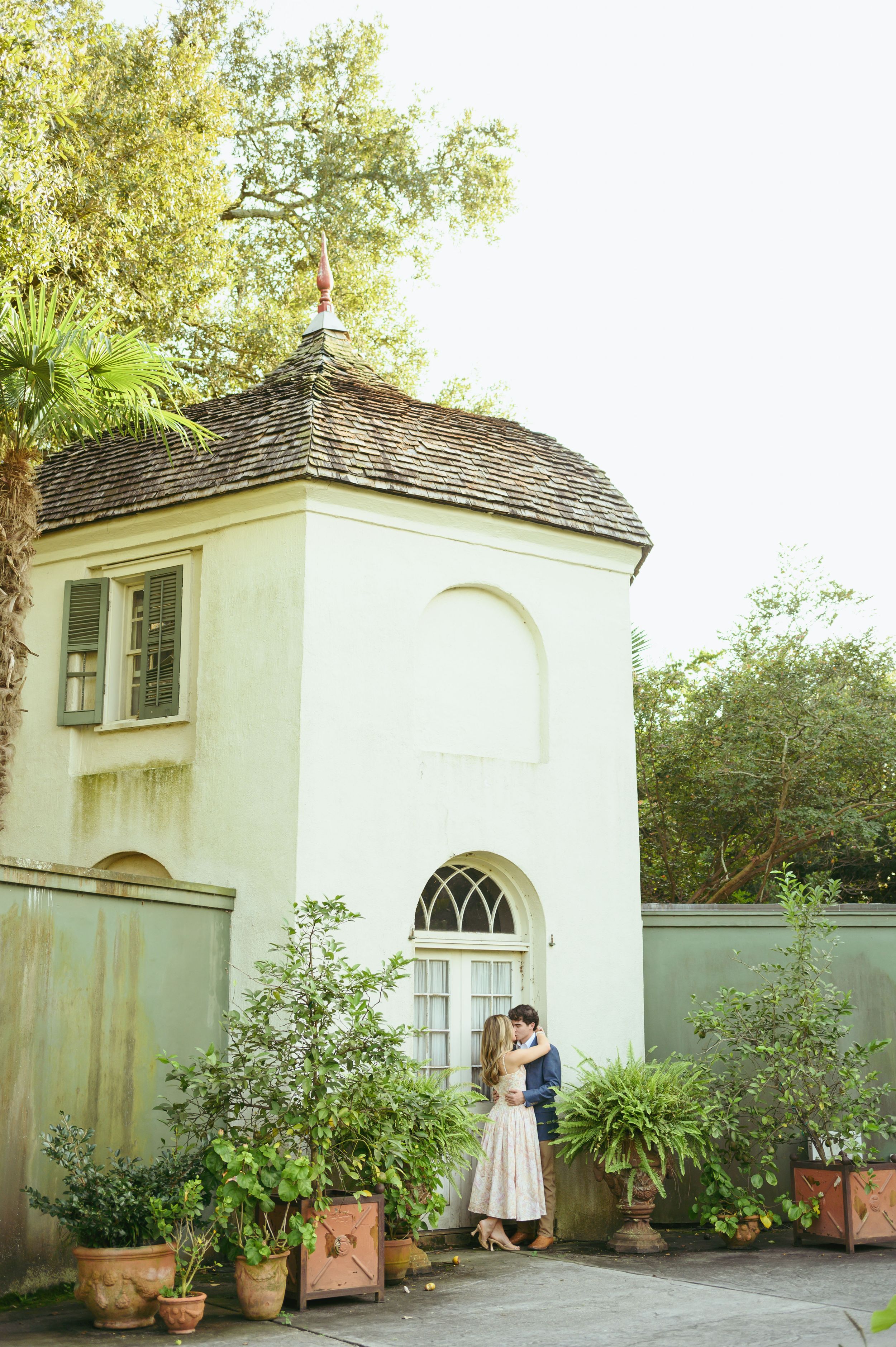 A charming white garden house with arched windows surrounded by potted plants and greenery at a historic estate.
