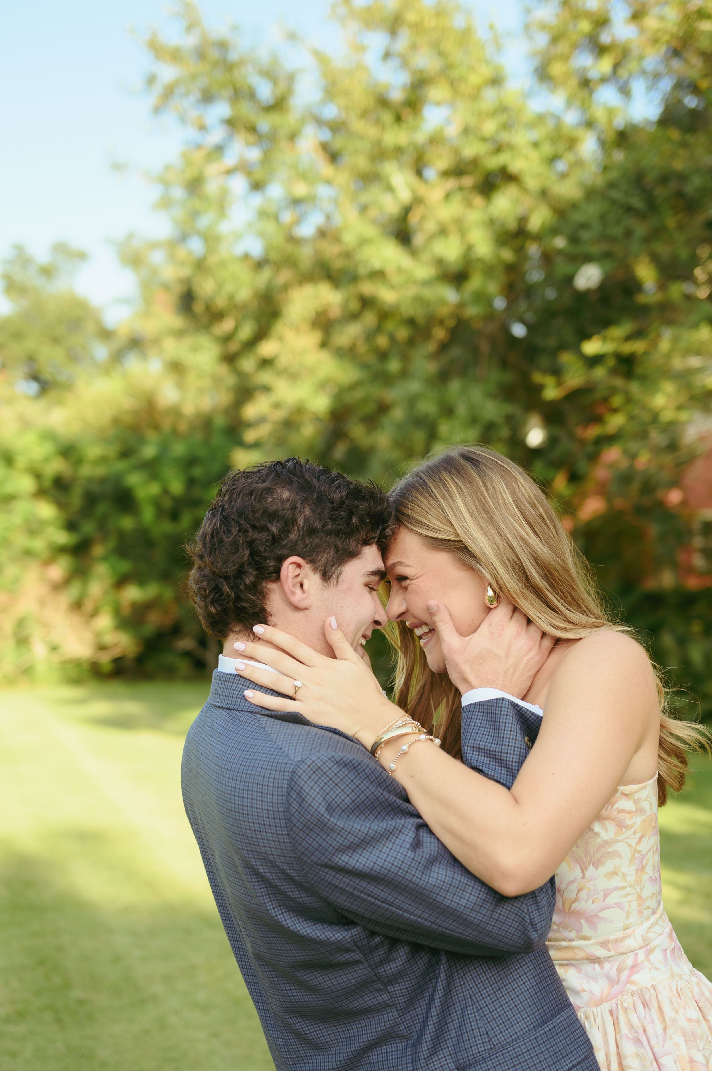 A joyful couple shares an intimate moment outdoors in a garden setting during what appears to be an engagement or wedding.