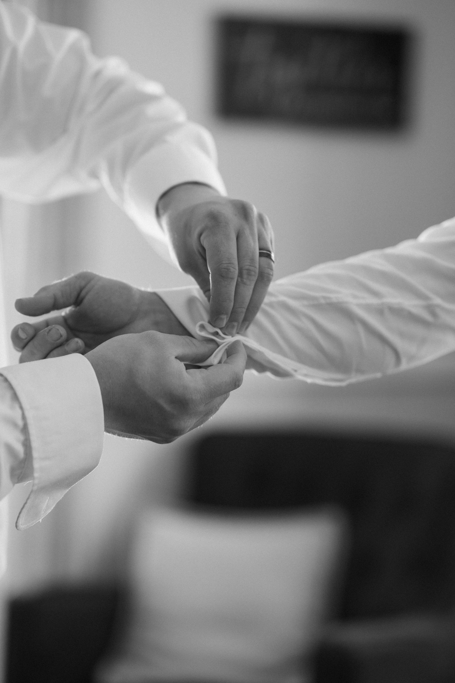 Black and white close-up of hands adjusting dress shirt cuffs with cufflinks.