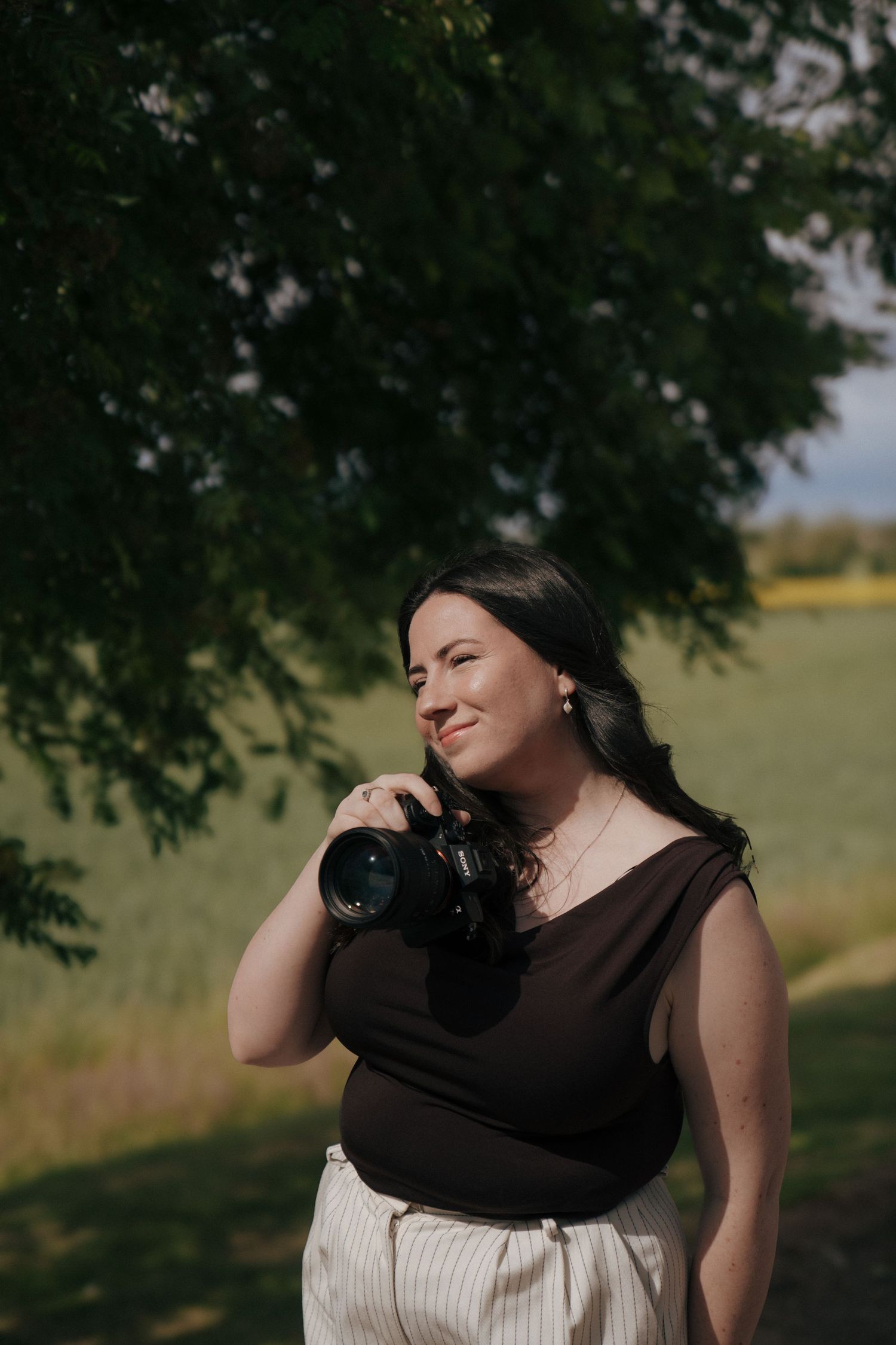 Portrait of photographer with professional camera under tree in natural outdoor setting.
