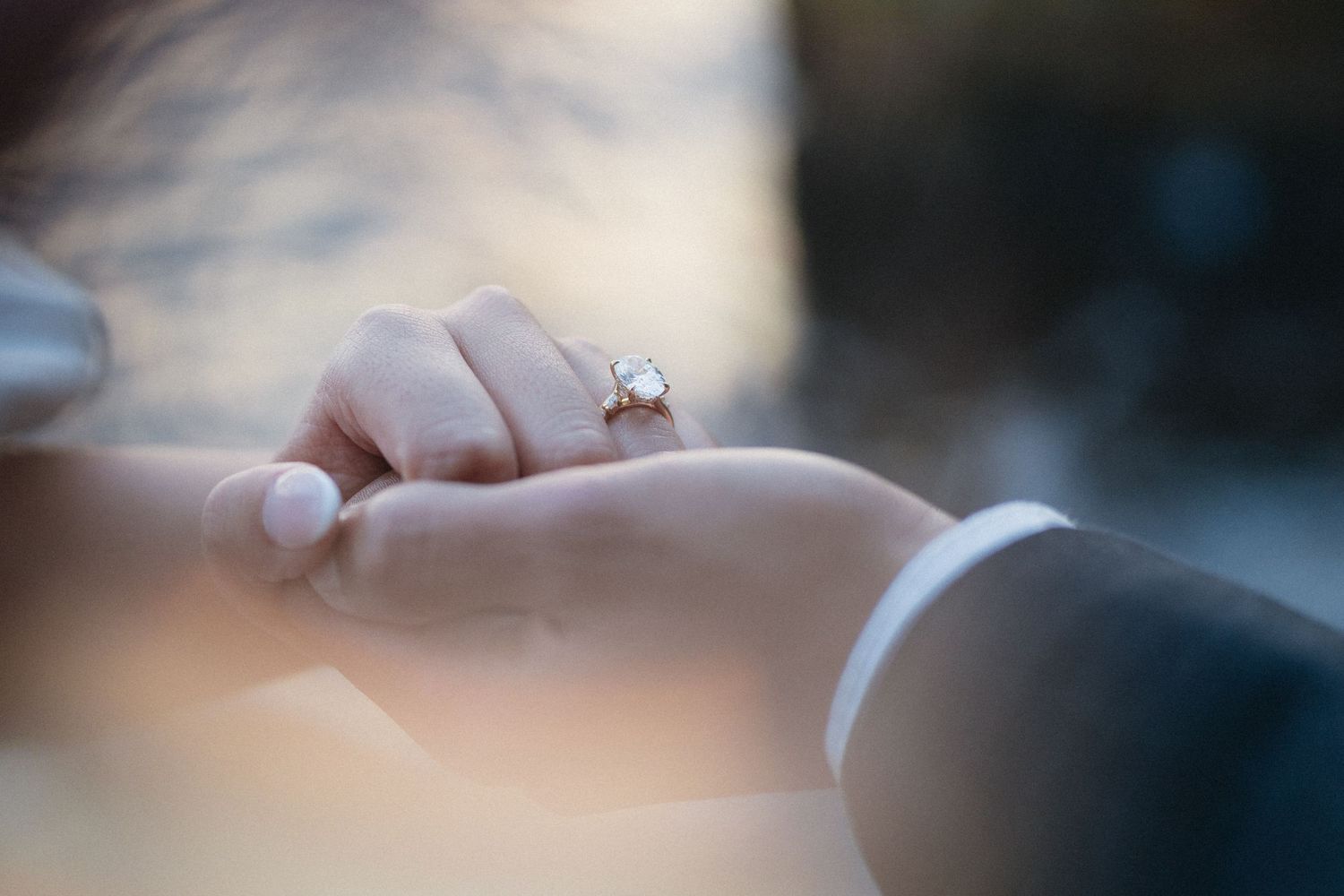 Close-up of hands joining together during romantic proposal with decorative lights and flowers.