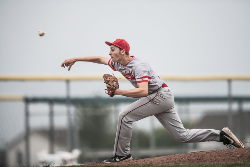 Baseball pitcher in gray uniform and red cap mid-throw on mound.