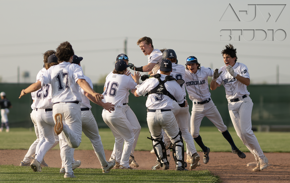 Baseball team celebrating victory with players jumping and hugging on field.