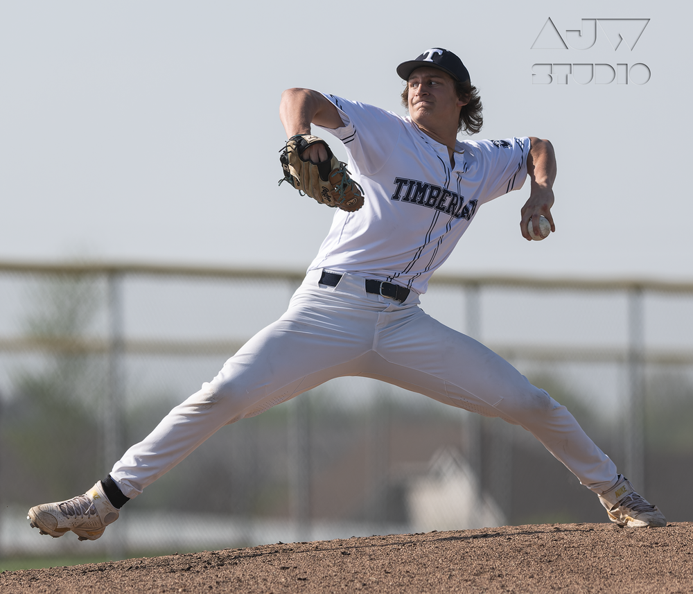 Baseball pitcher in mid-delivery motion on pitcher's mound wearing white uniform.