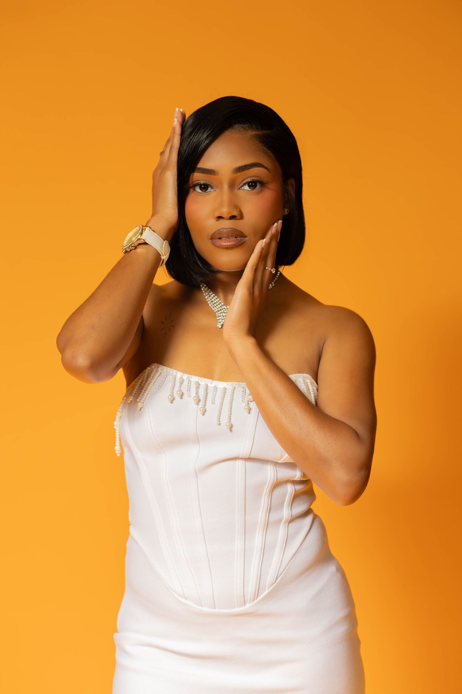 Young Black woman in white corset dress poses gracefully against a vibrant orange background.