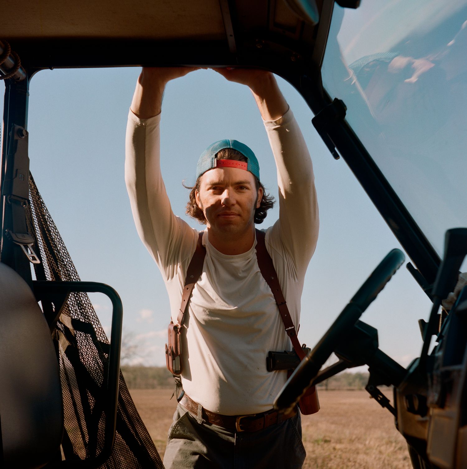 Man wearing gun holster and a white shirt reaching up on his gator looking into the camera