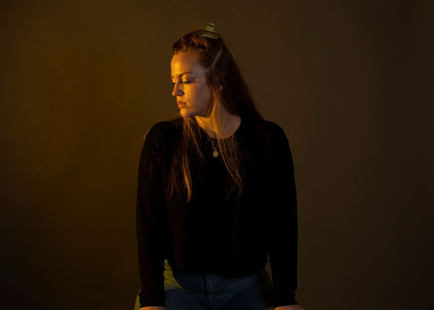 Dramatic side profile portrait of a person in a dark sweater illuminated by warm ambient lighting against a dark background.