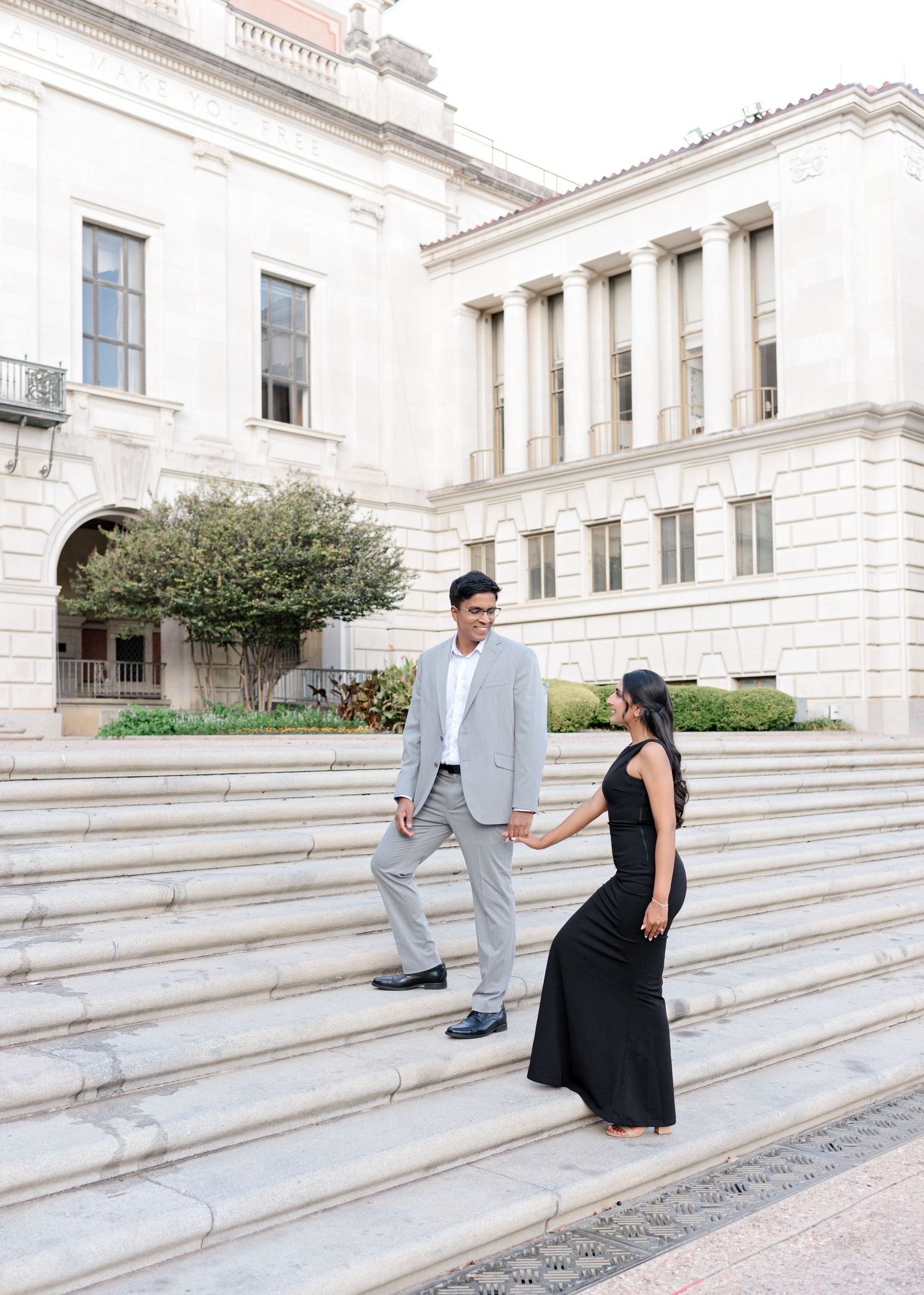 engaged couple walking up stairs while holding hands and looking at each other at the University of Texas