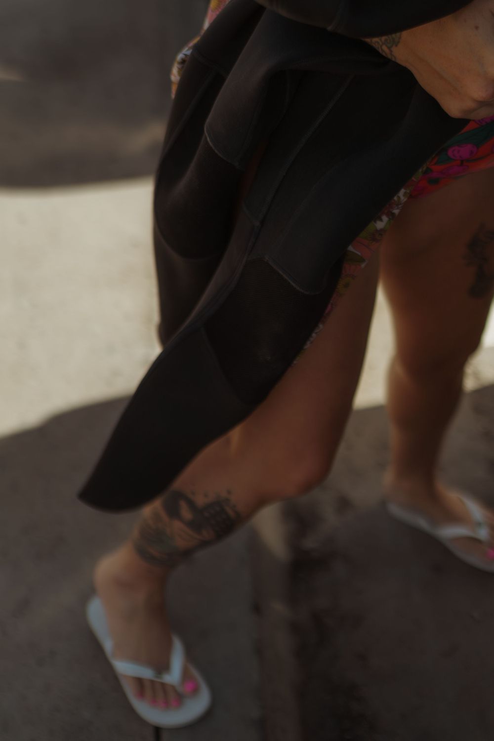 Close-up of legs wearing flip flops with a wetsuit draped over them.