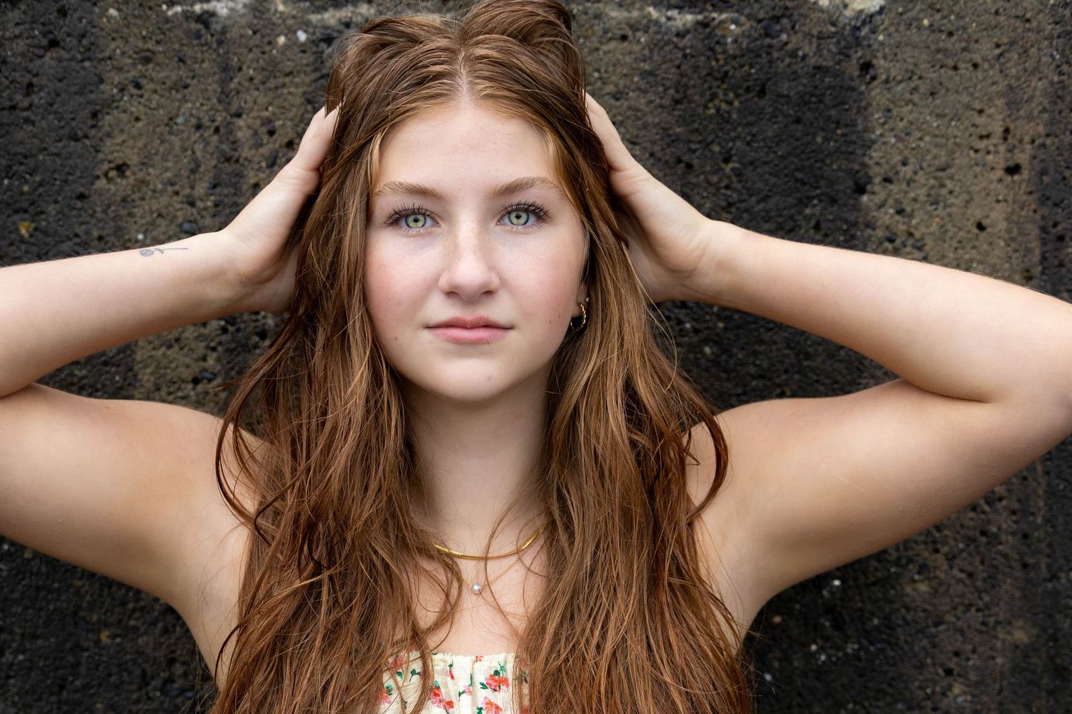 A portrait of a young woman with wet hair running fingers through her hair against a dark background.