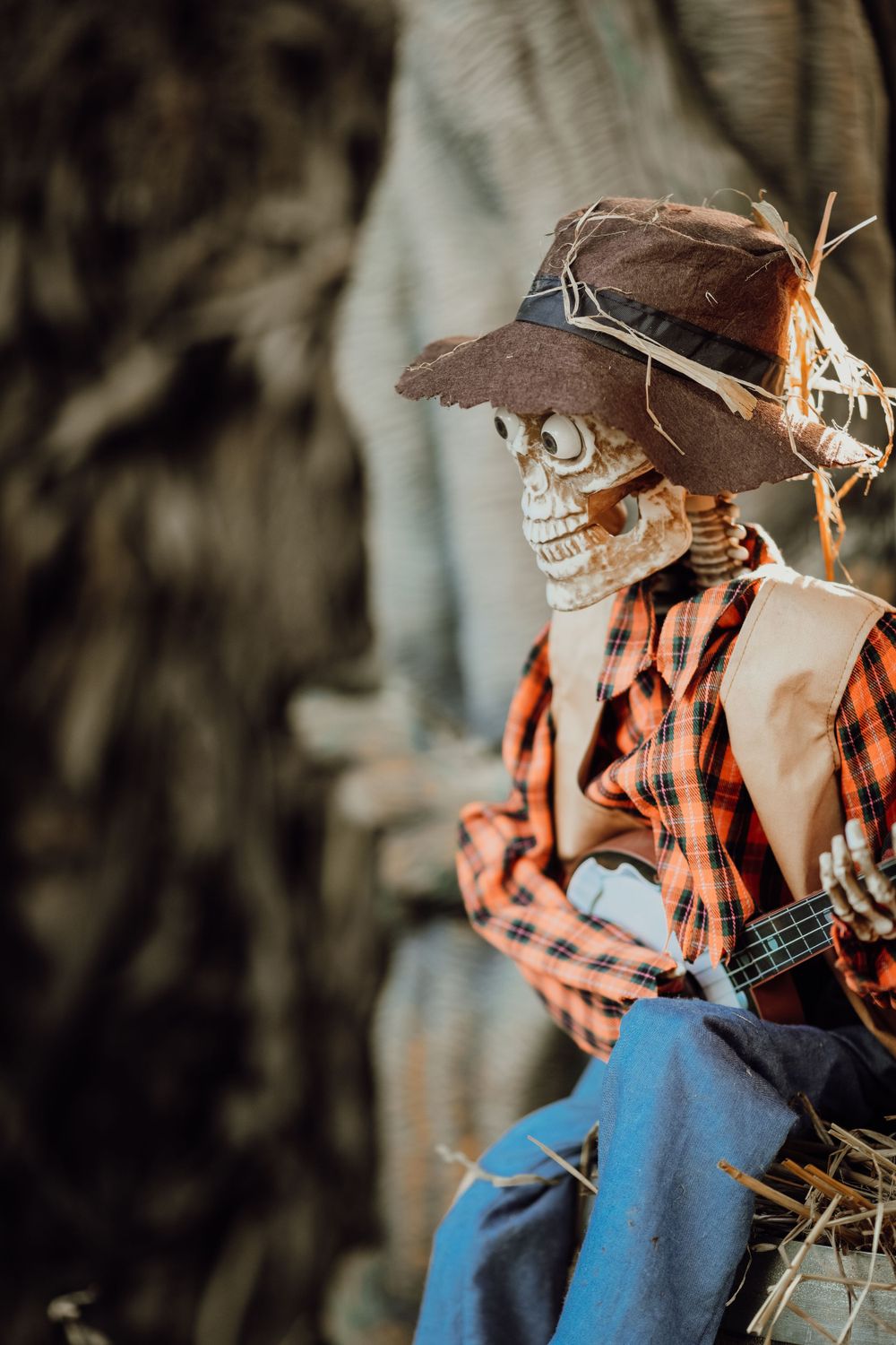 Halloween decoration of a skeleton wearing cowboy attire sitting on hay bales.