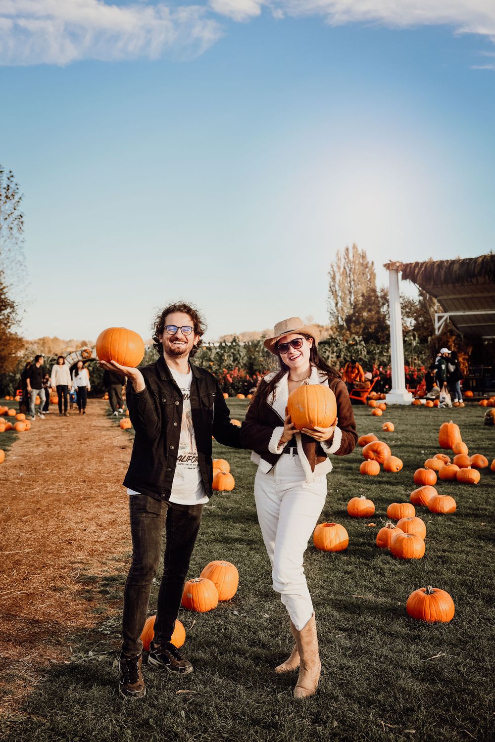 Happy couple holding pumpkins at a fall pumpkin patch on a sunny autumn day.