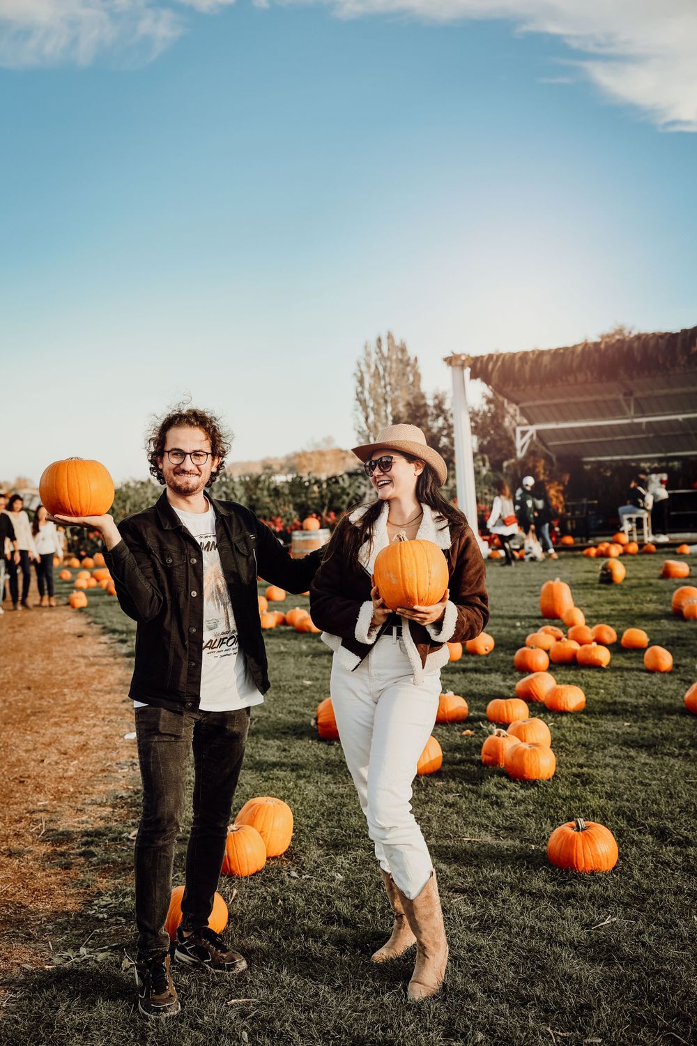 Two people posing with pumpkins at an autumn farm festival.
