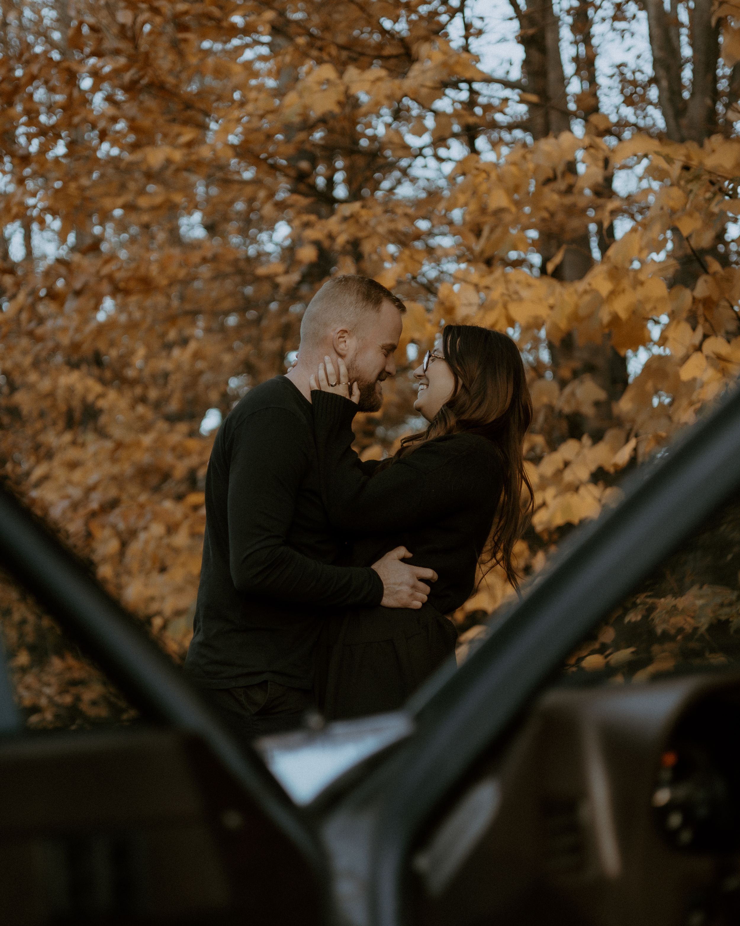 Romantic couple embracing against fall foliage backdrop.