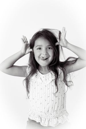Black and white portrait of a playful young girl with long hair sticking out her tongue and holding her hands up like horns.