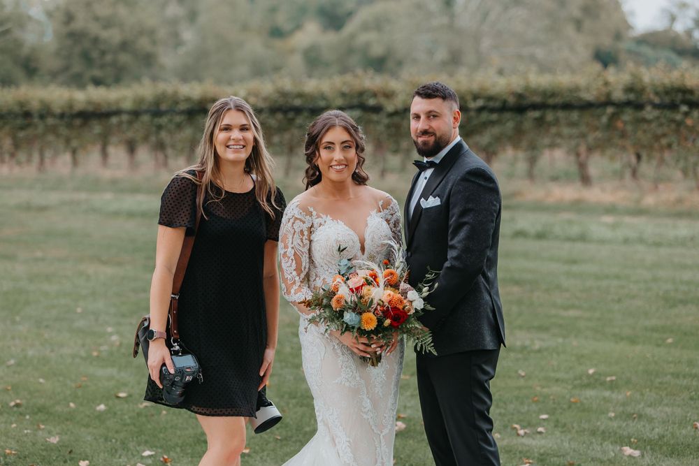 Wedding party of three poses outdoors with autumn-colored floral bouquet.