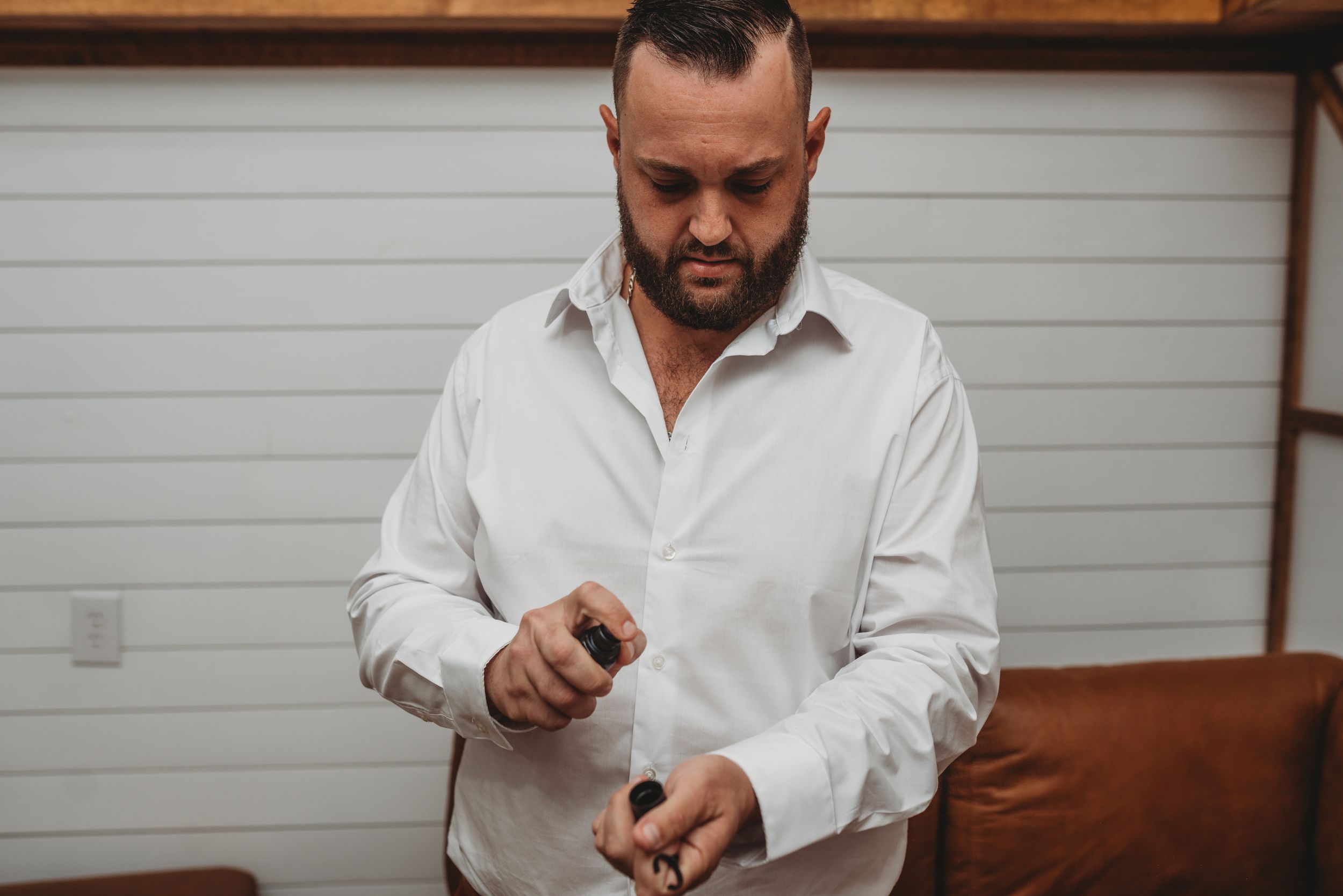 Person in white button-down shirt opens small gift box while standing by couch.