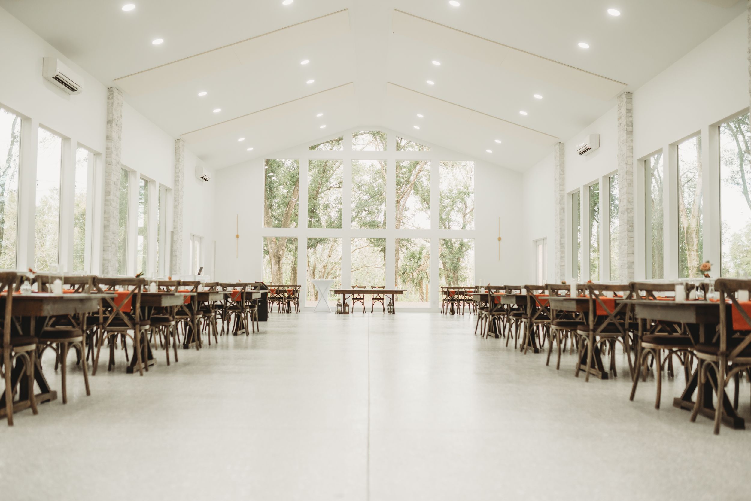 Modern white wedding venue with wooden chairs and large windows filled with natural light.