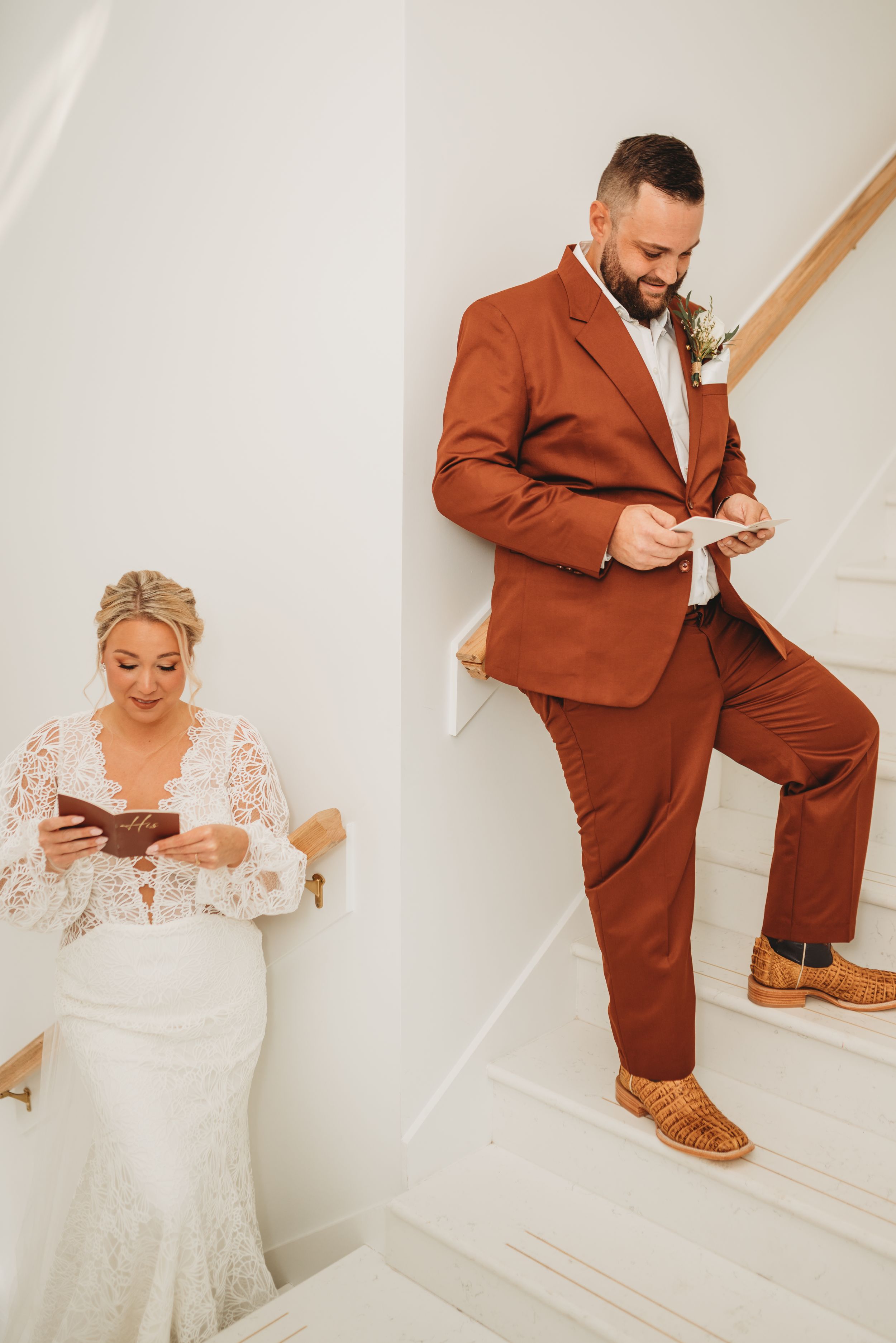 Couple reading letters separately before wedding ceremony on white staircase.